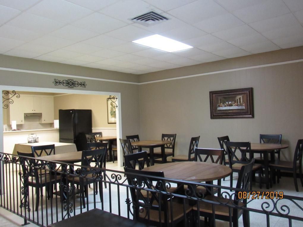 Dining area with round tables and chairs, beige walls, kitchen in the background, decorative railing.