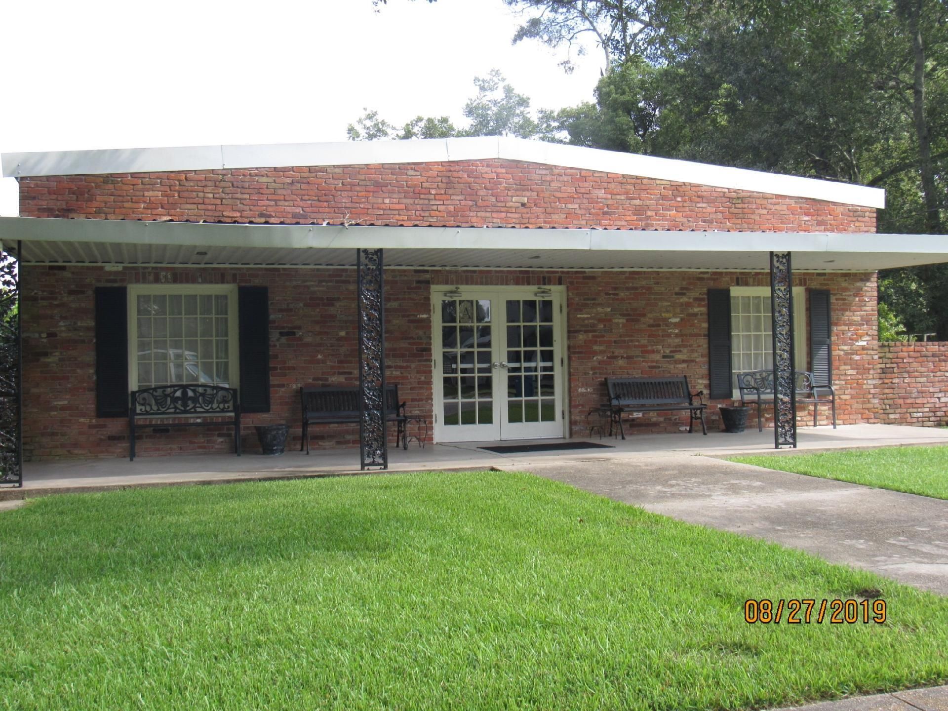 Brick building with a covered porch, white double doors, and black shutters, set in a grassy yard.