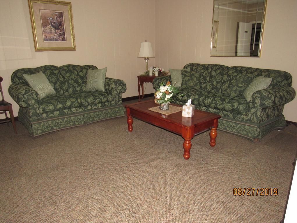 Two green floral sofas facing each other in a room with a brown coffee table, lamp, and mirror.