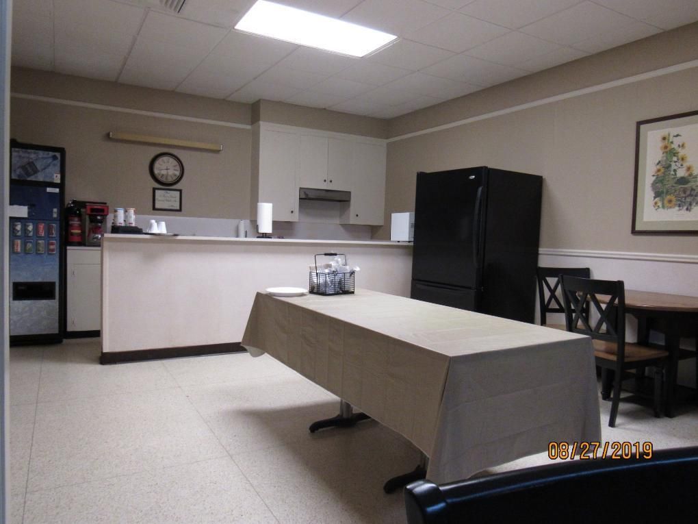 A small kitchen/break room with a large table, cabinets, a fridge, and vending machine.