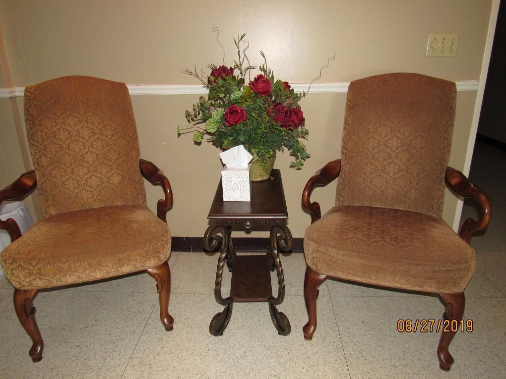 Two brown upholstered chairs flank a small table with a floral arrangement.