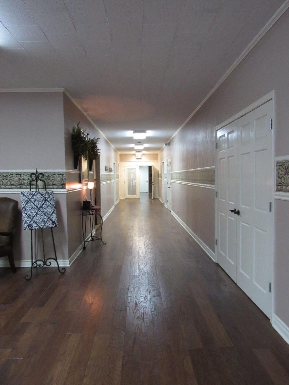 Long hallway with wooden floor, pink walls, and white doors.
