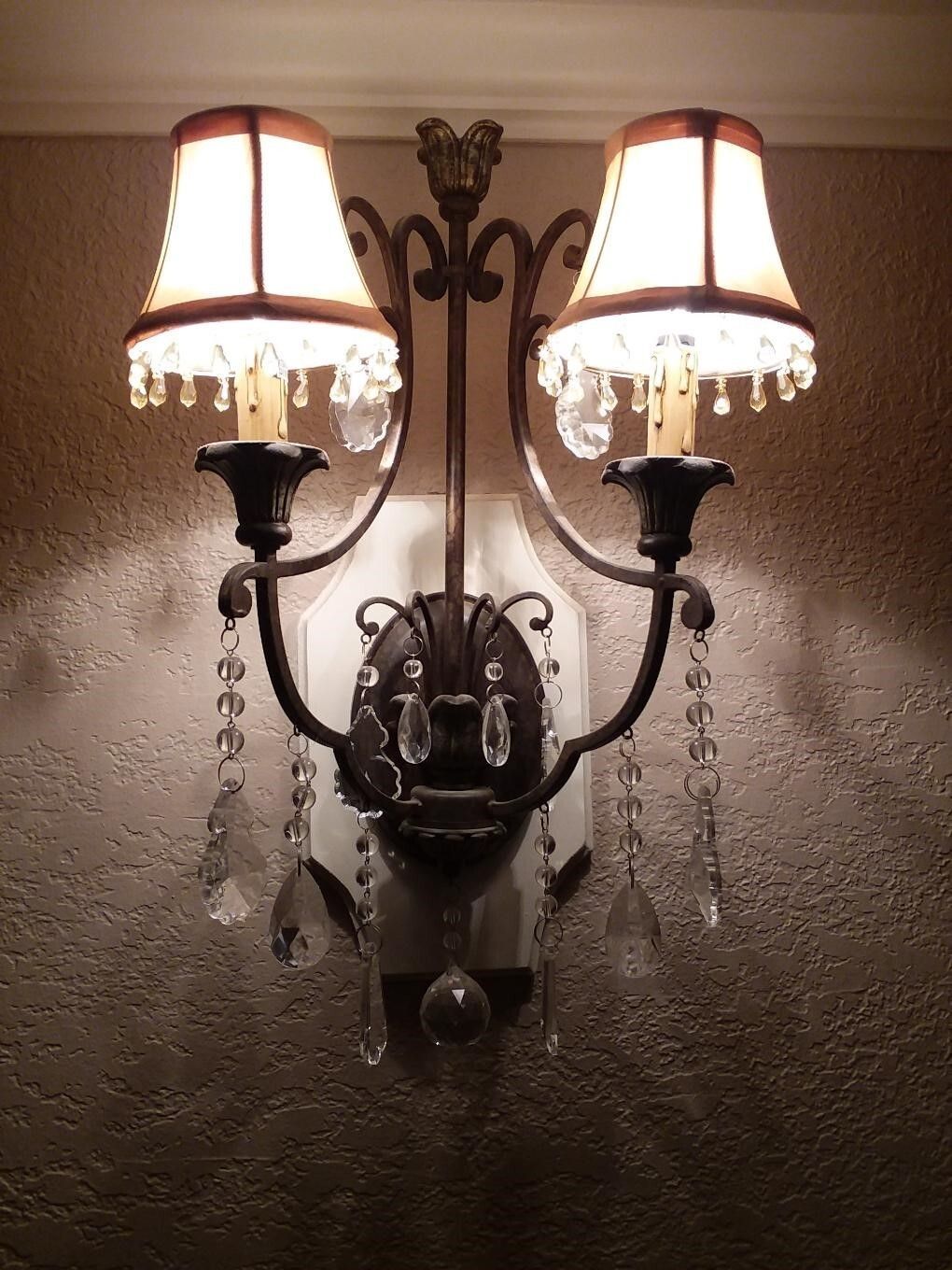 Wall-mounted two-light sconce with lampshades, ornate metalwork, and hanging crystals.