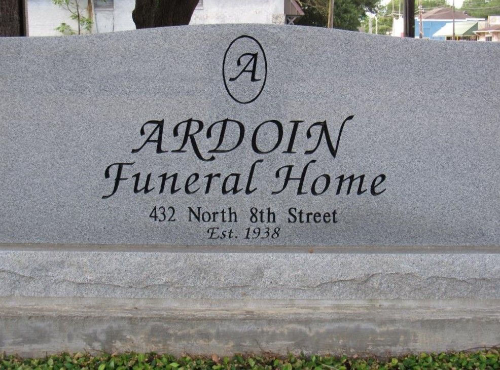 Sign for Ardoin Funeral Home, grey stone, black lettering, address, and established date.