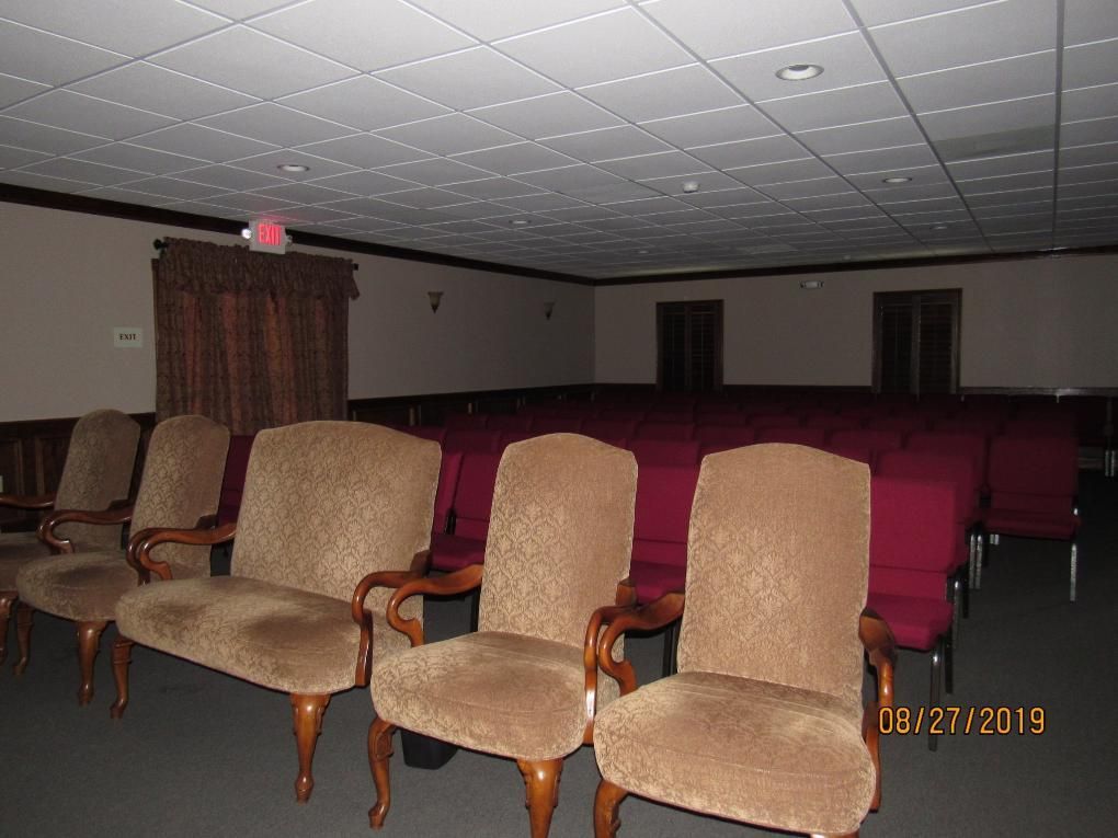 Rows of chairs in a dimly lit room, with brown armchairs in front and red chairs in the back.