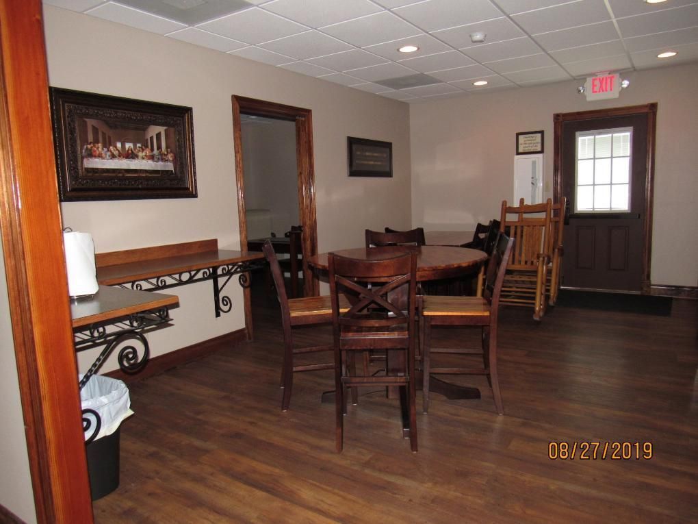 Interior room with a table, chairs, artwork, and a doorway. Wooden floor and neutral-toned walls.