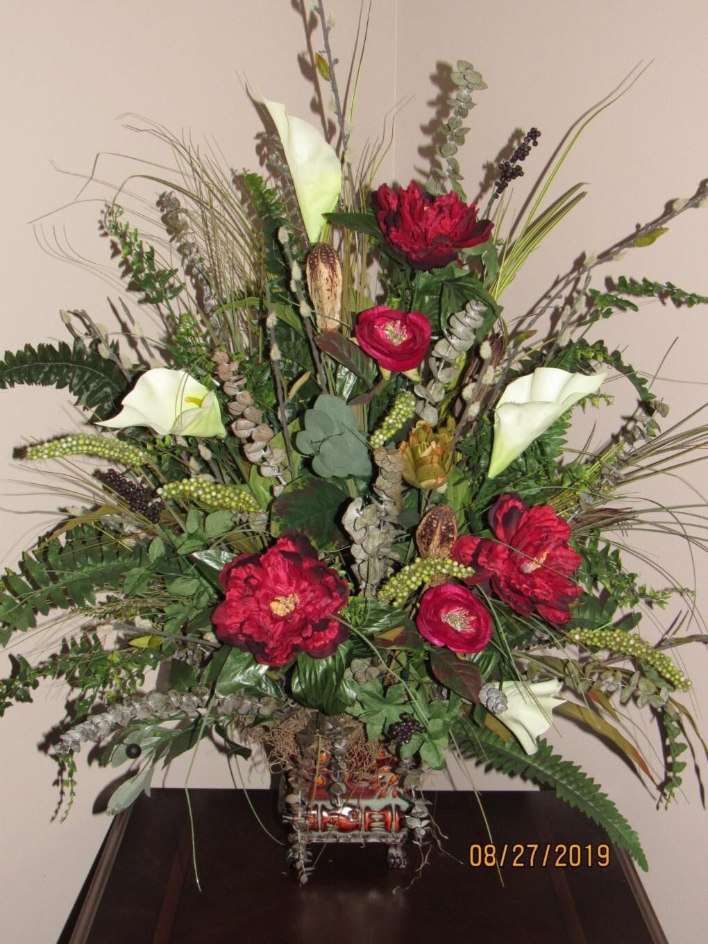 Floral arrangement in a decorative basket, featuring red flowers, white calla lilies, and greenery.