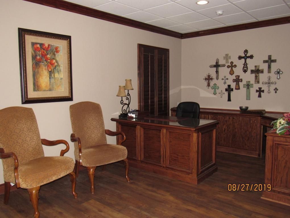 An office with brown wooden furniture, tan walls, and a collection of crosses on the wall.