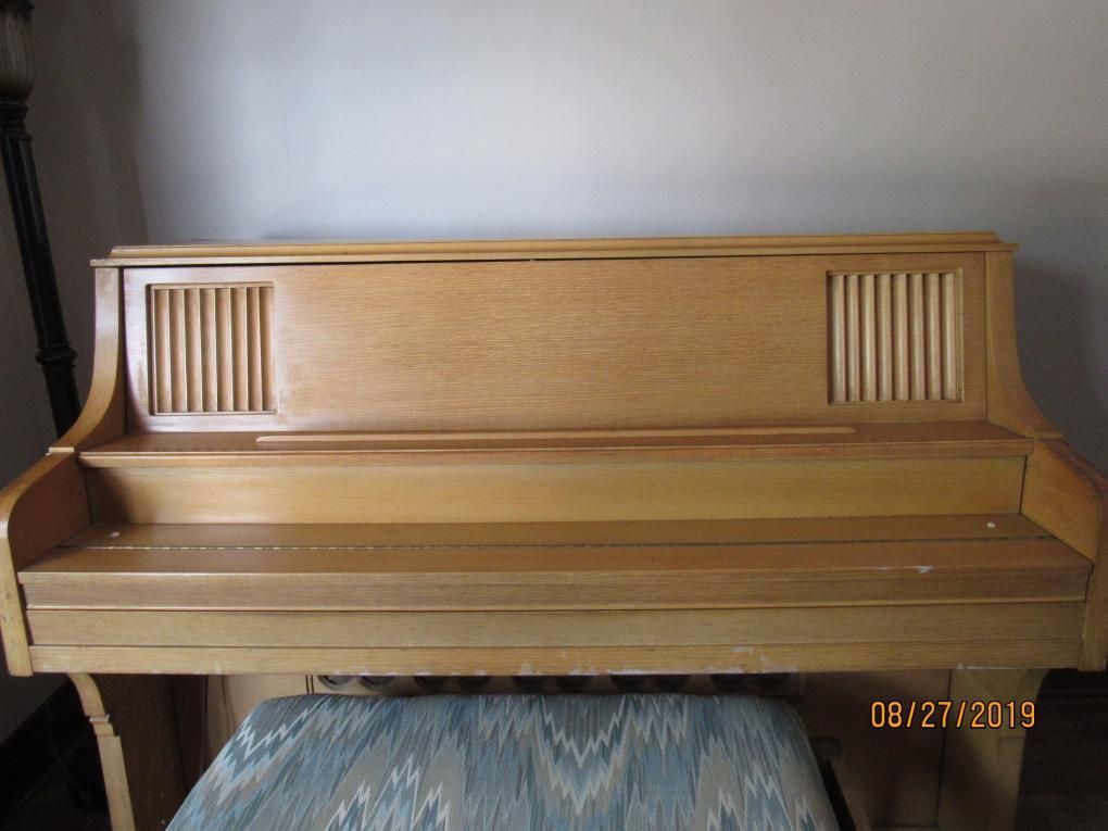 Light wood upright piano with decorative slats on the back, and a blue patterned piano bench.