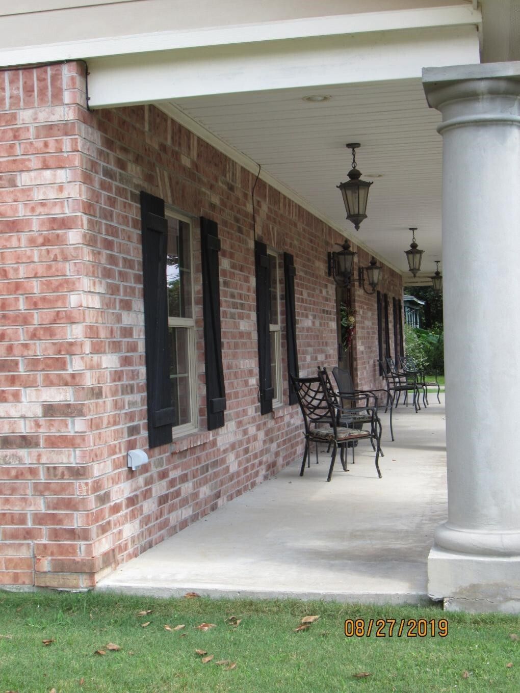 Brick building with a covered porch. Black shutters, chairs, and hanging lanterns.