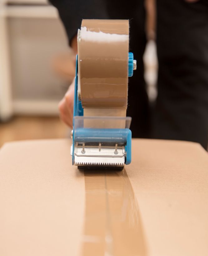 A Person is Using a Tape Dispenser to Tape a Box — Dunford Removals in Miriam Vale, QLD