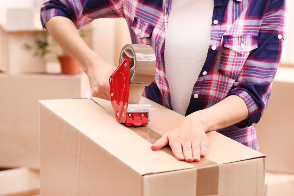 A Woman is Taping a Cardboard Box With Tape — Dunford Removals in Woodgate, QLD