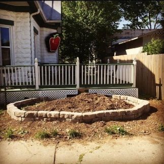 A brick-lined, circular garden bed sits in front of a white building with a red apple sign.