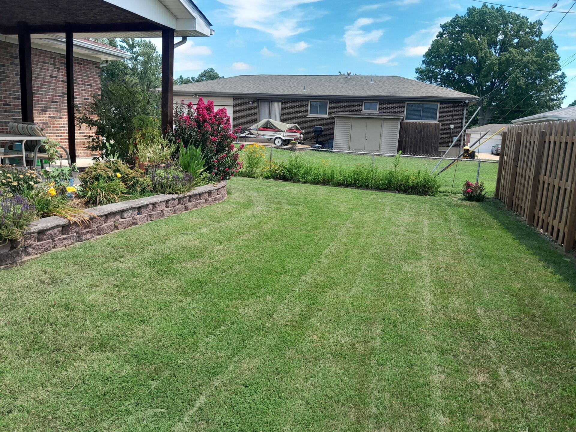 A well-manicured backyard with a brick retaining wall, green grass, and a house in the background.