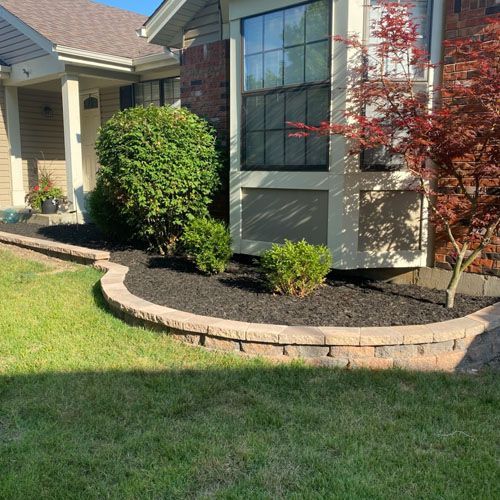 House with a retaining wall, garden bed with mulch, and vibrant greenery.