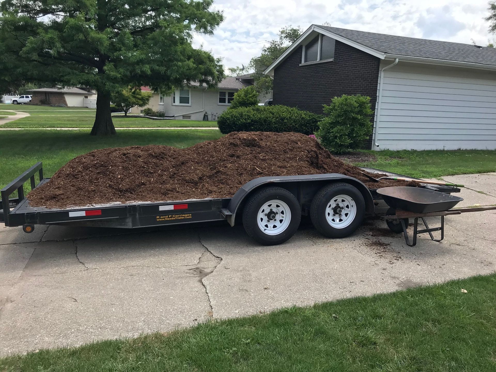 Person watering newly planted garden rows with a hose. A potato with sprouts is held in the foreground.