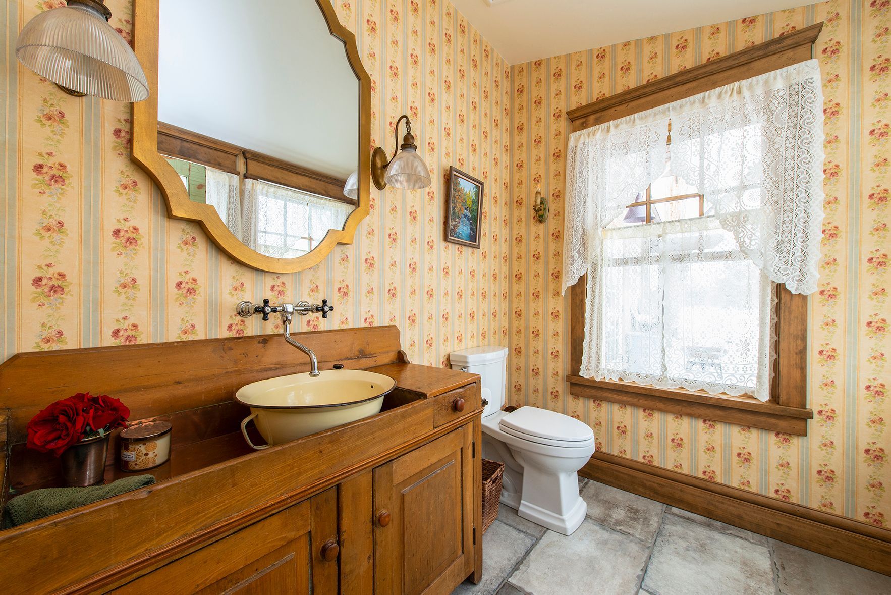 A bathroom with a sink , toilet , mirror and window.