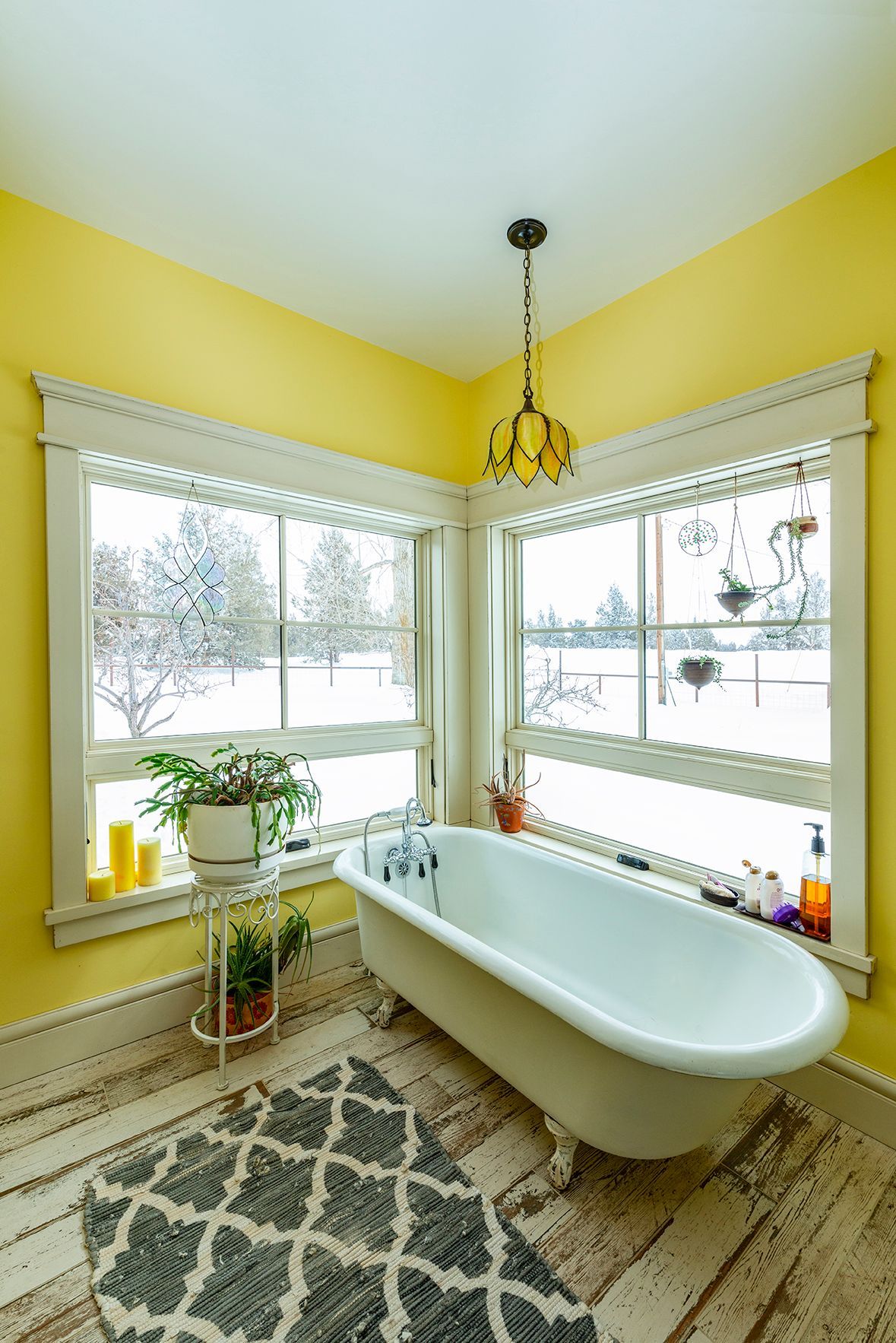 A bathroom with yellow walls and a bathtub in front of a window.