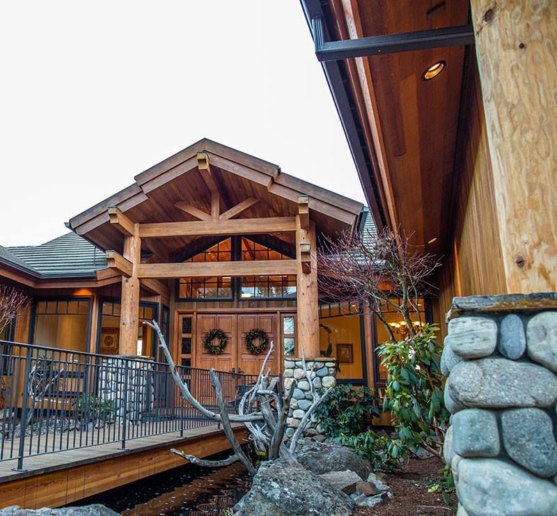 A large wooden house with a stone wall in front of it