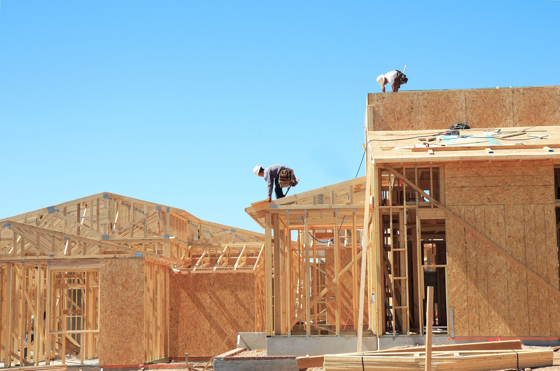 Construction workers building wooden house frames under blue sky.