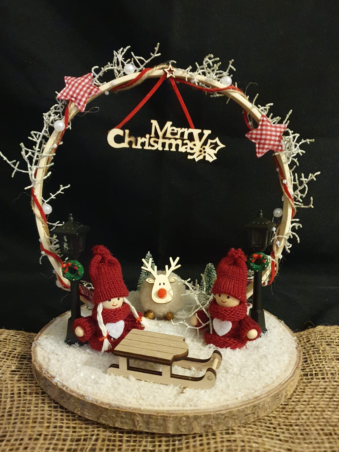 Couronne de Noël ornée de décorations rouges, d'une pancarte « Joyeux Noël » et de petites figurines festives sur un socle 