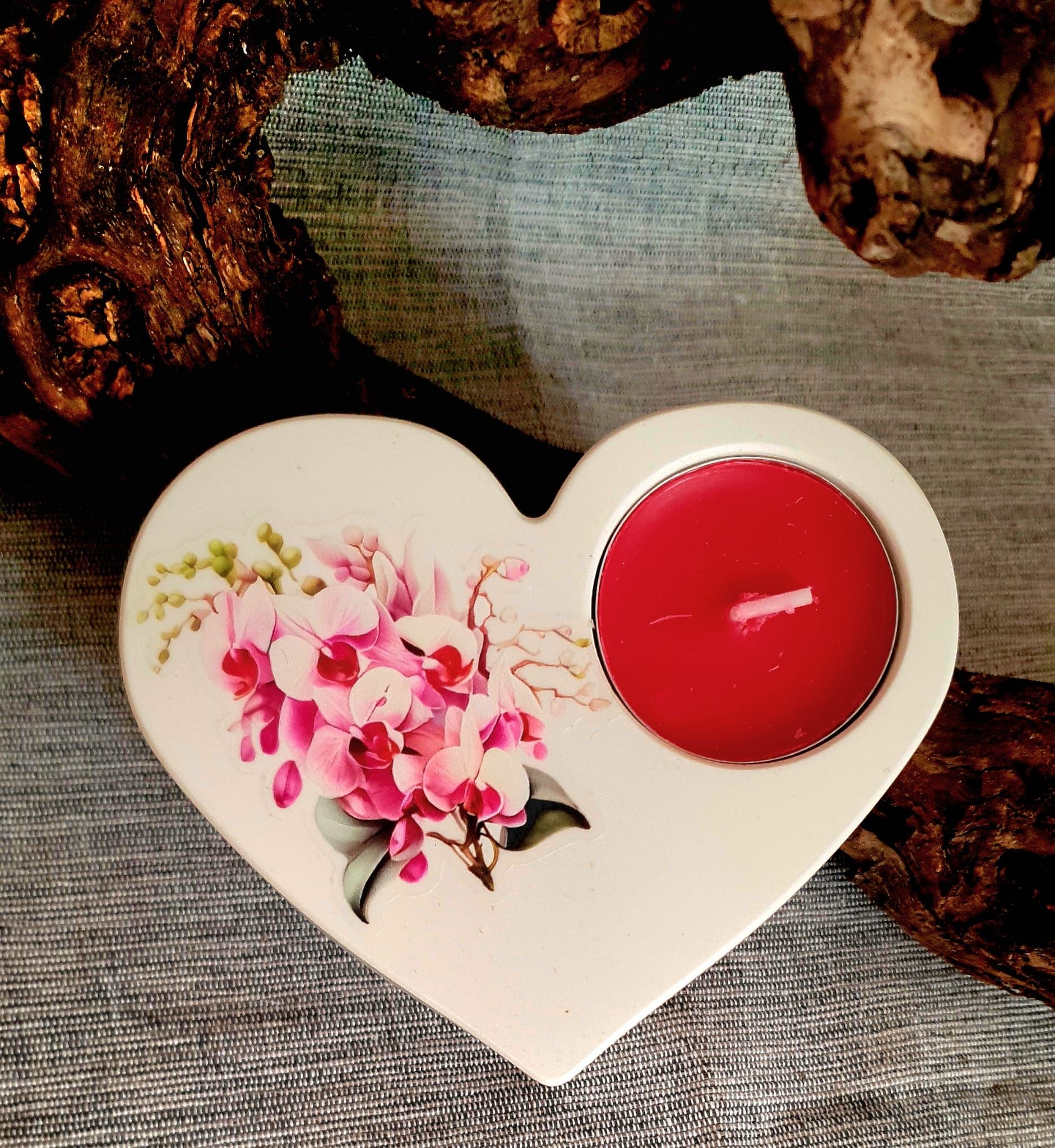 Bougeoir floral en forme de cœur avec une bougie rouge sur une surface texturée, encadré de bois foncé