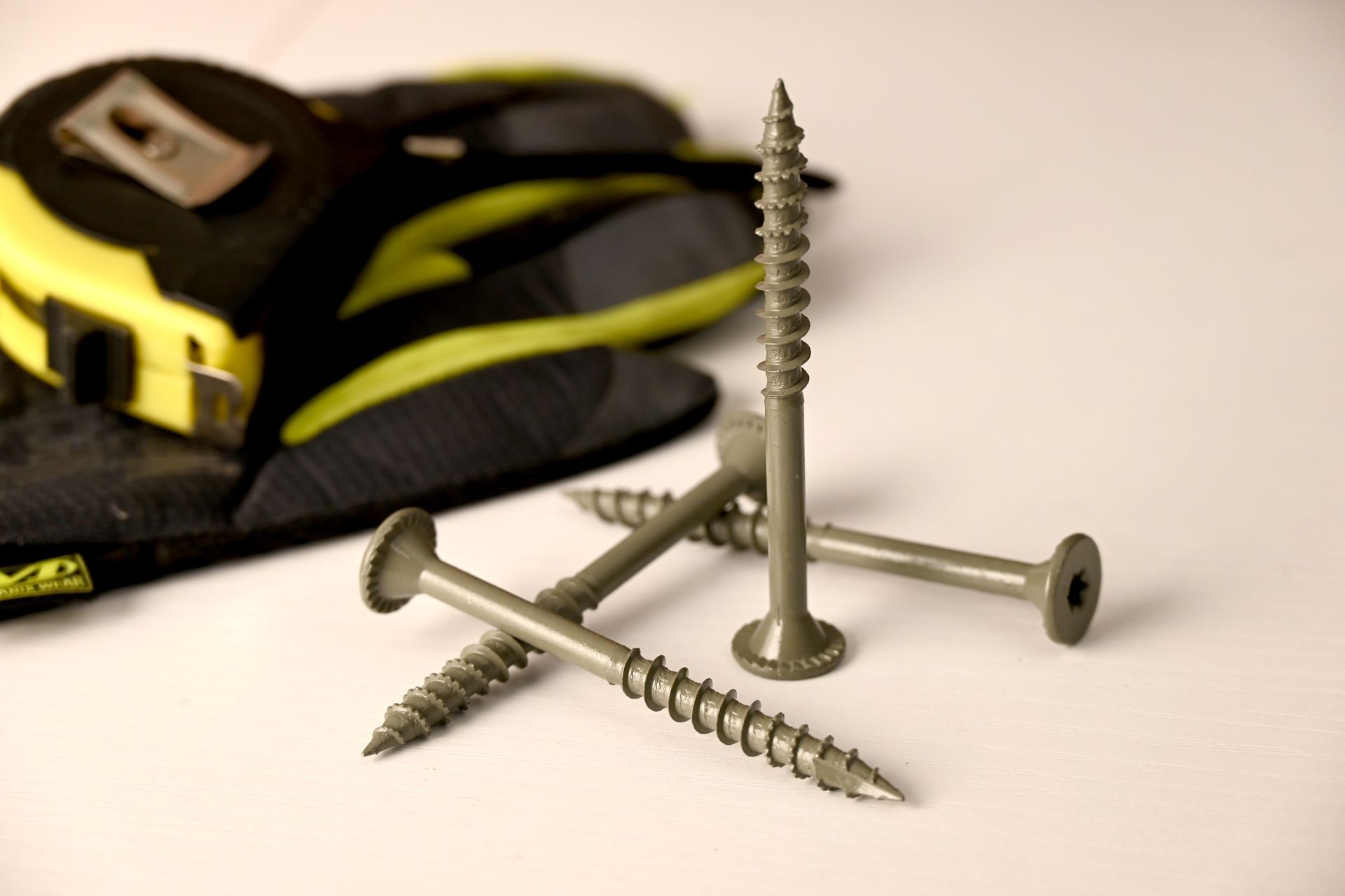 Three silver screws in front of a yellow-and-black tool belt on a white surface