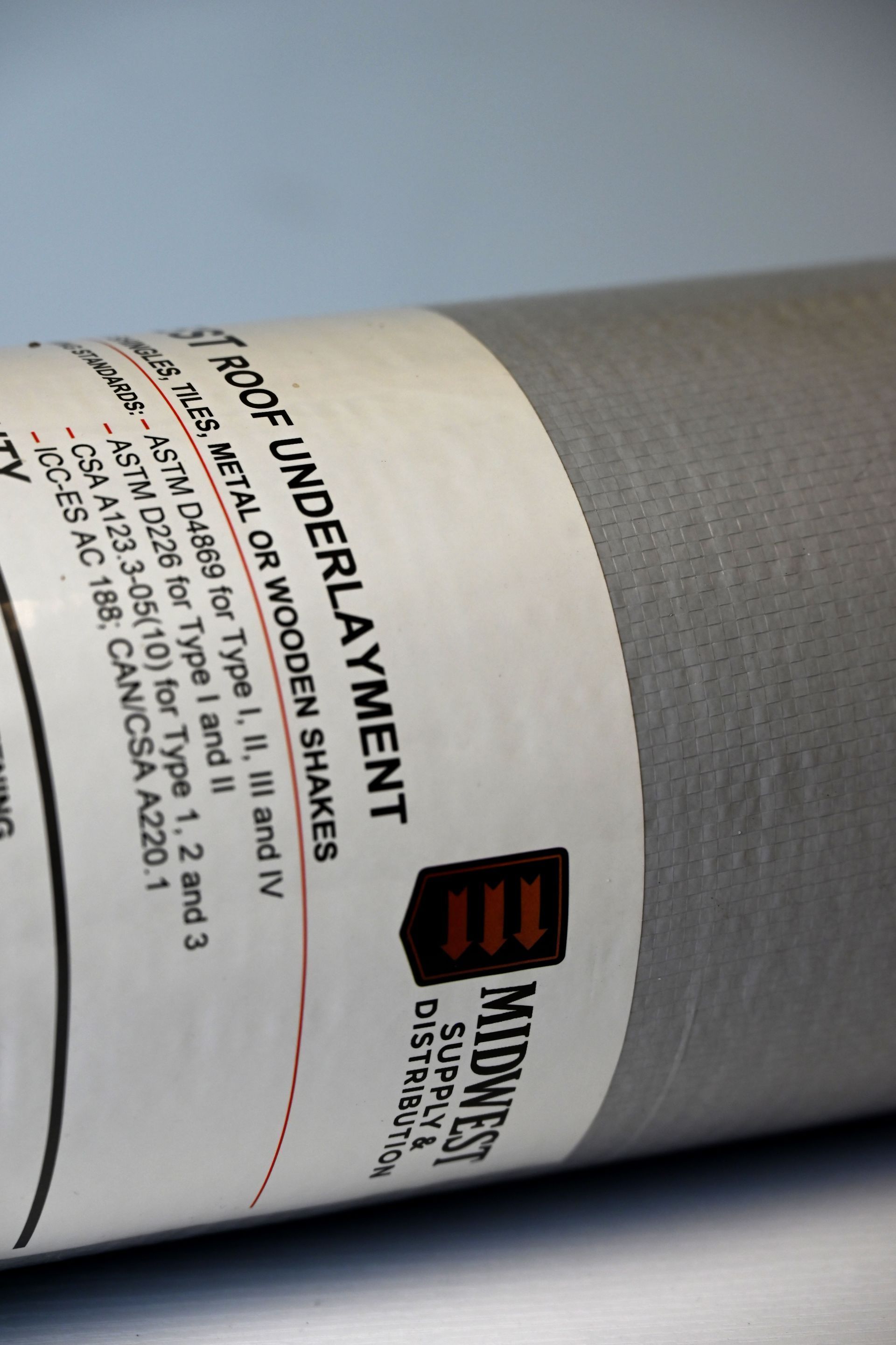 Roll of black anti-skid underlayment with a white product label on a gray background