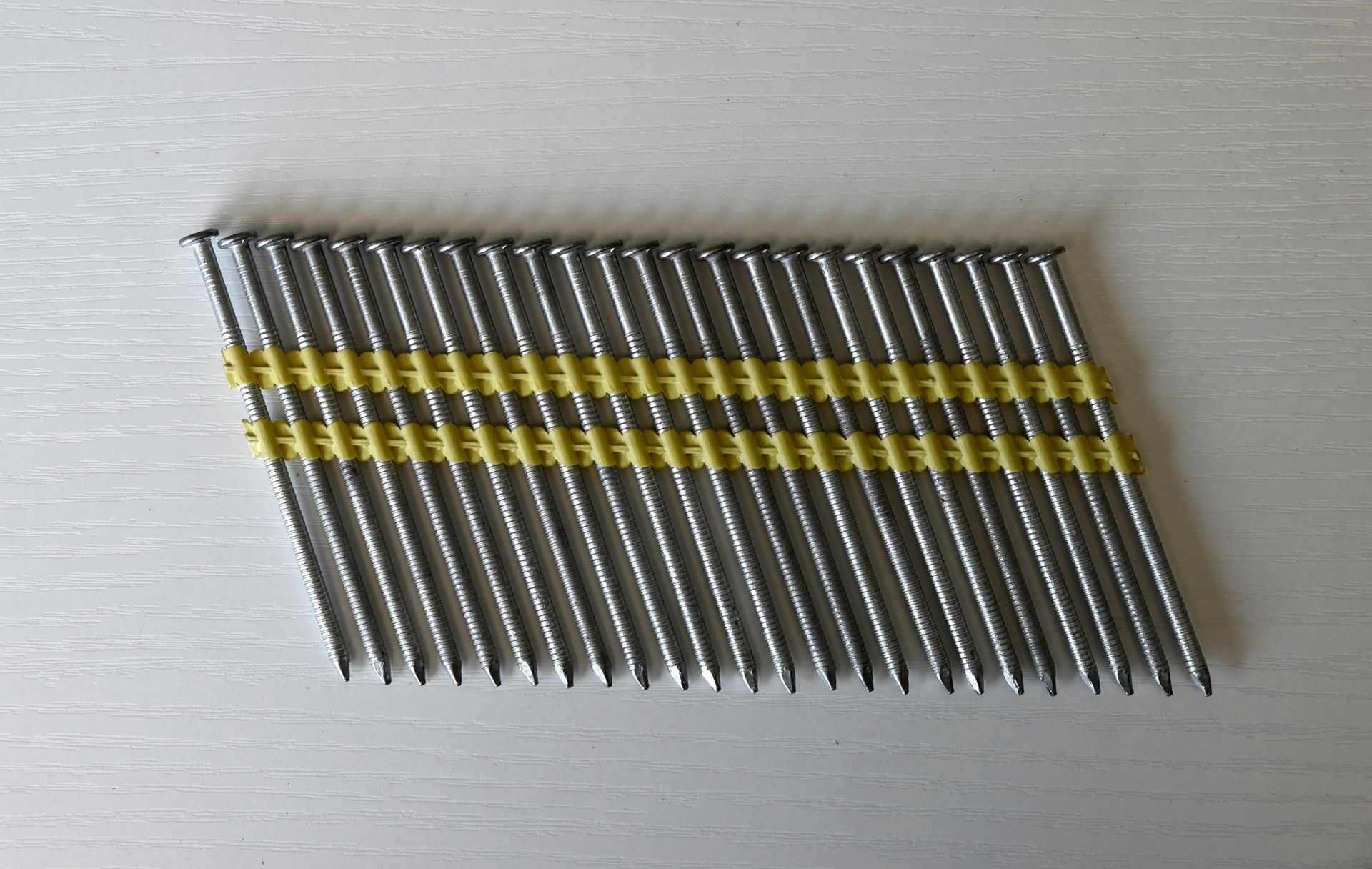 A bundle of metal nails with yellow bands, arranged diagonally on a light surface.