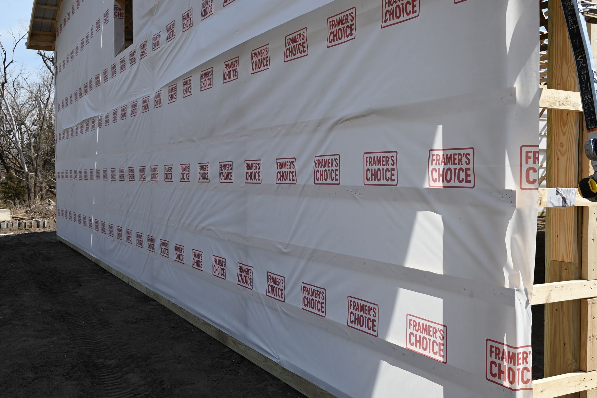 Wrapped building materials beside a wooden frame, covered in white protective sheeting with red branding.