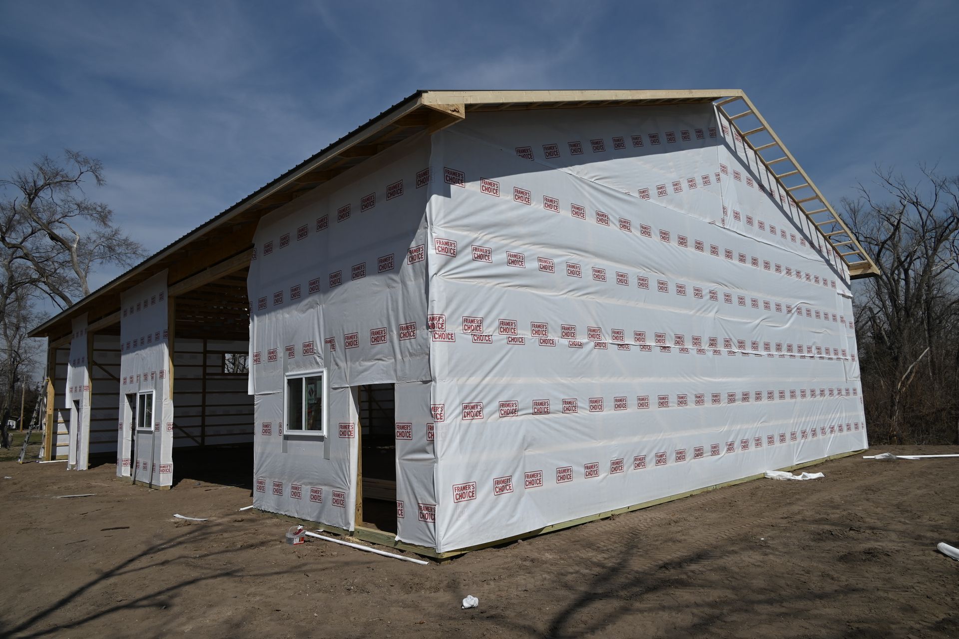 Partially wrapped white house under construction with a large open garage and dirt yard
