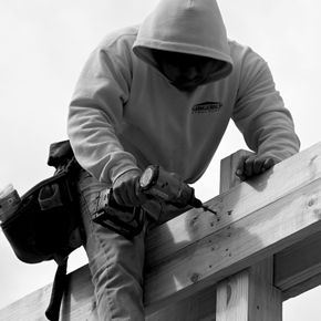 Worker in a hooded sweatshirt using a power drill on a roof beam