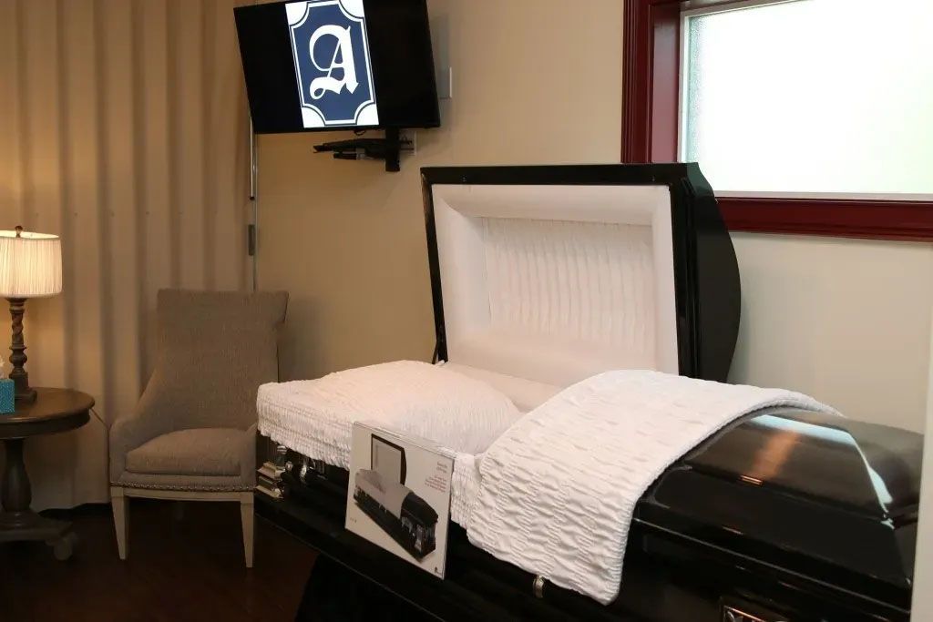 A black coffin is open in a room with a chair and a television.