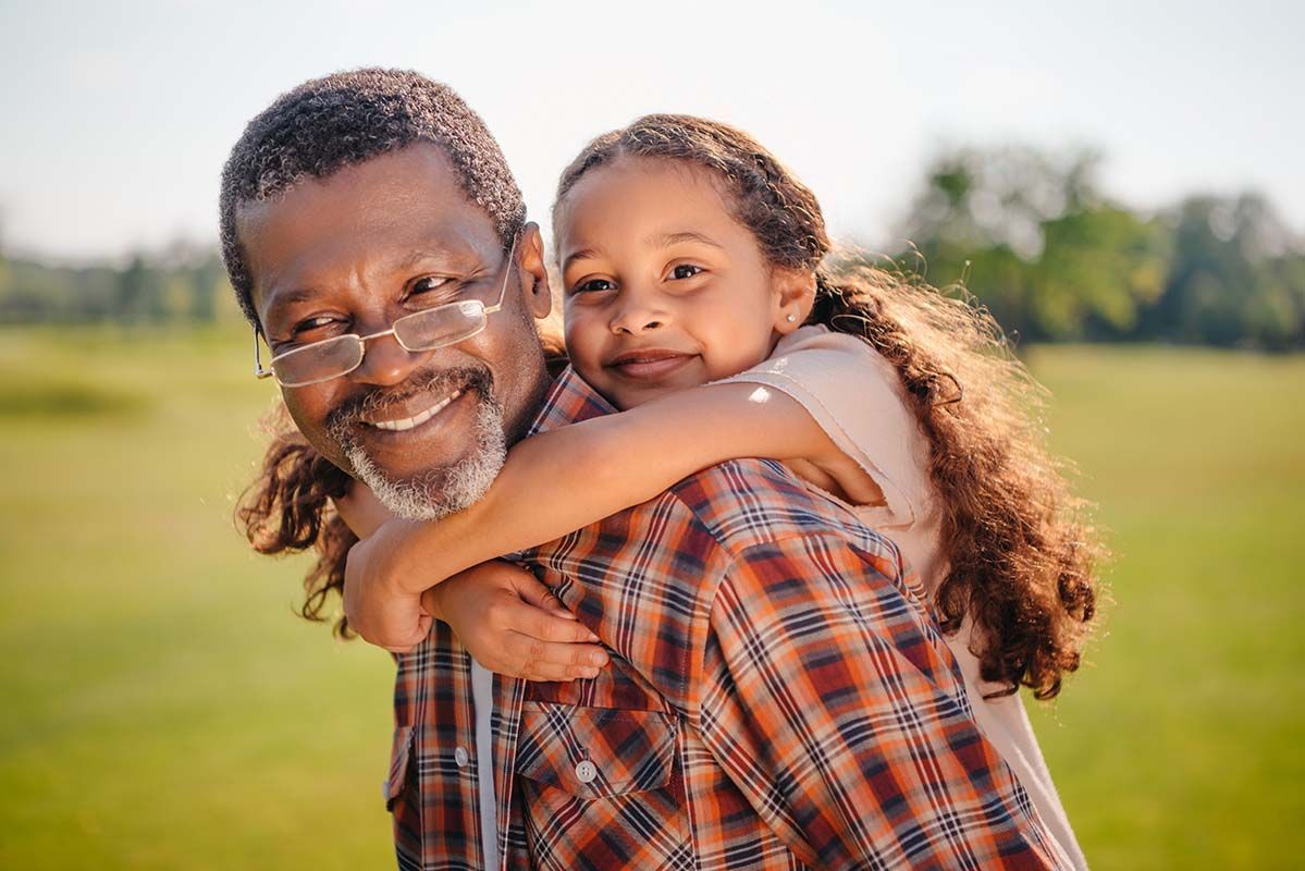 A man is carrying a little girl on his shoulders in a field.