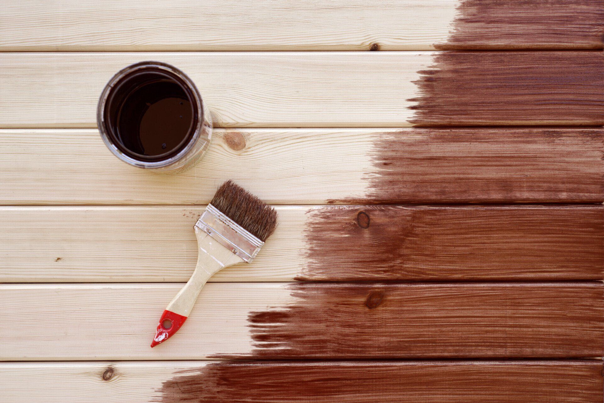 An image of a wooden surface with half of it painted, revealing brush strokes and a can of paint nearby.