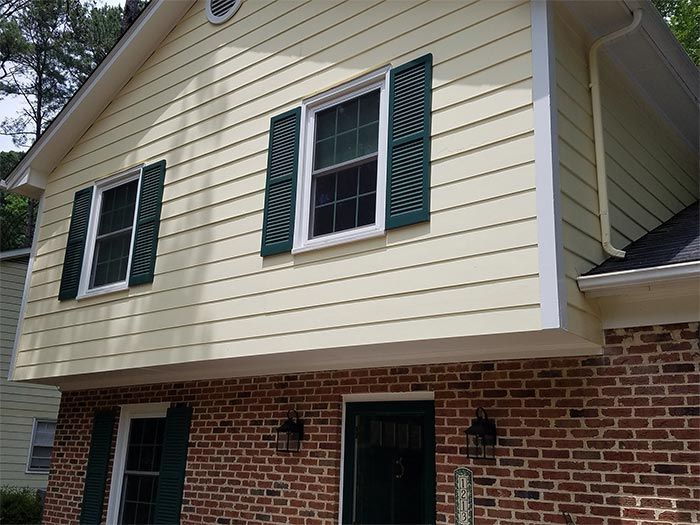 Two-story house with yellow siding and dark green shutters over brick.
