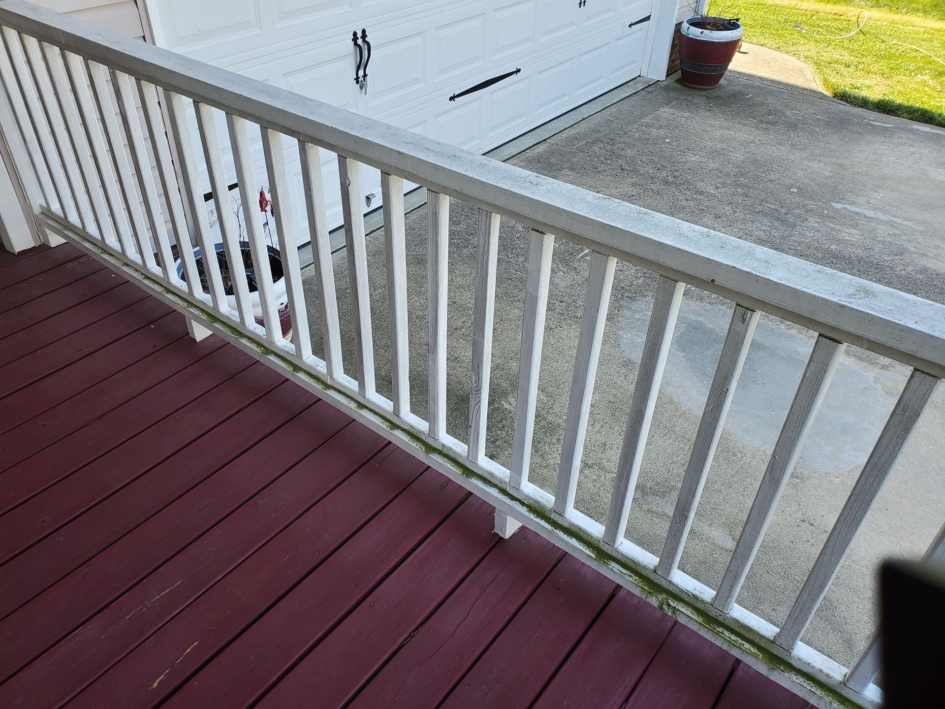 White railing on a dark red porch, overlooking a driveway and garage. Green algae on the railing.