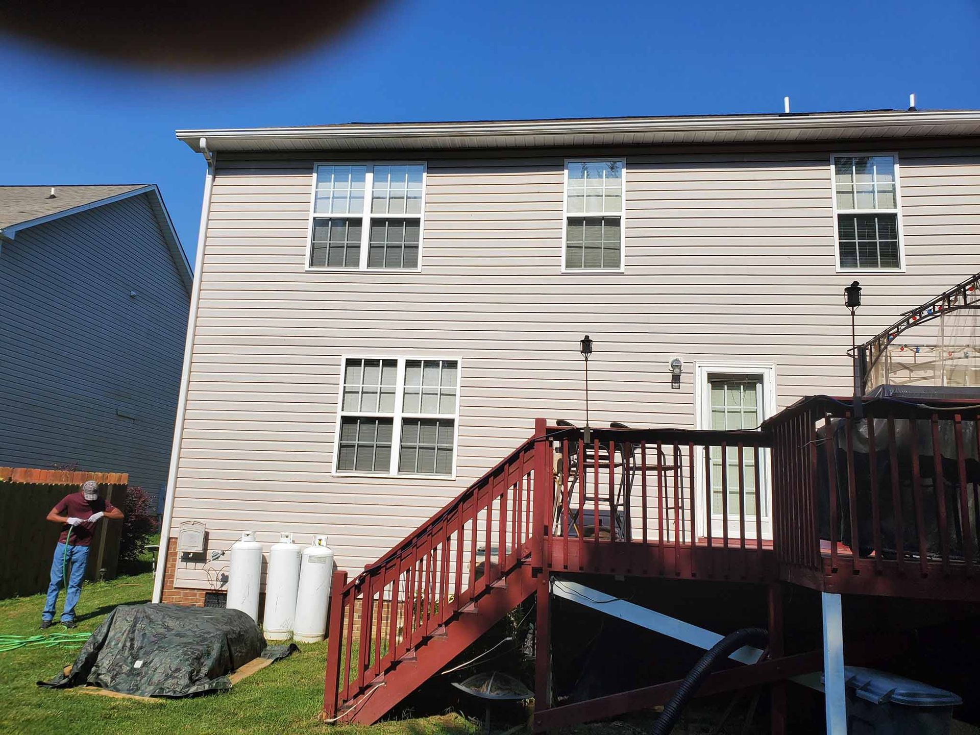 Back of a two-story house with a deck, propane tanks, and a person in the yard.