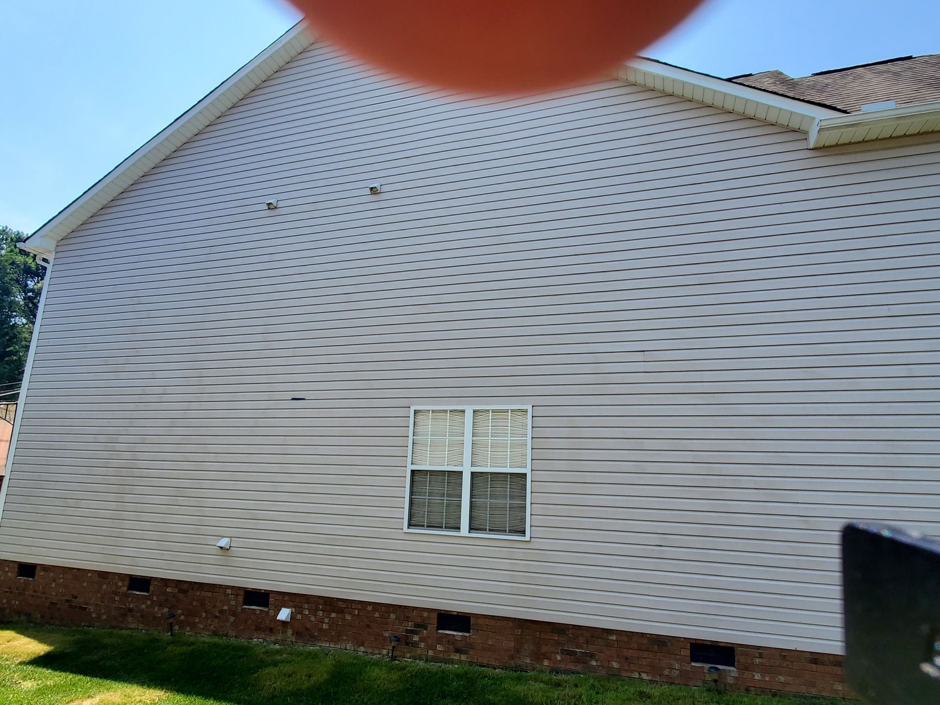 Side of a house with white siding, a window, and a brick foundation; bright sunlight.