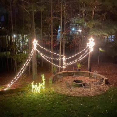Lit Christmas lights in a backyard with a fire pit and reindeer decorations.