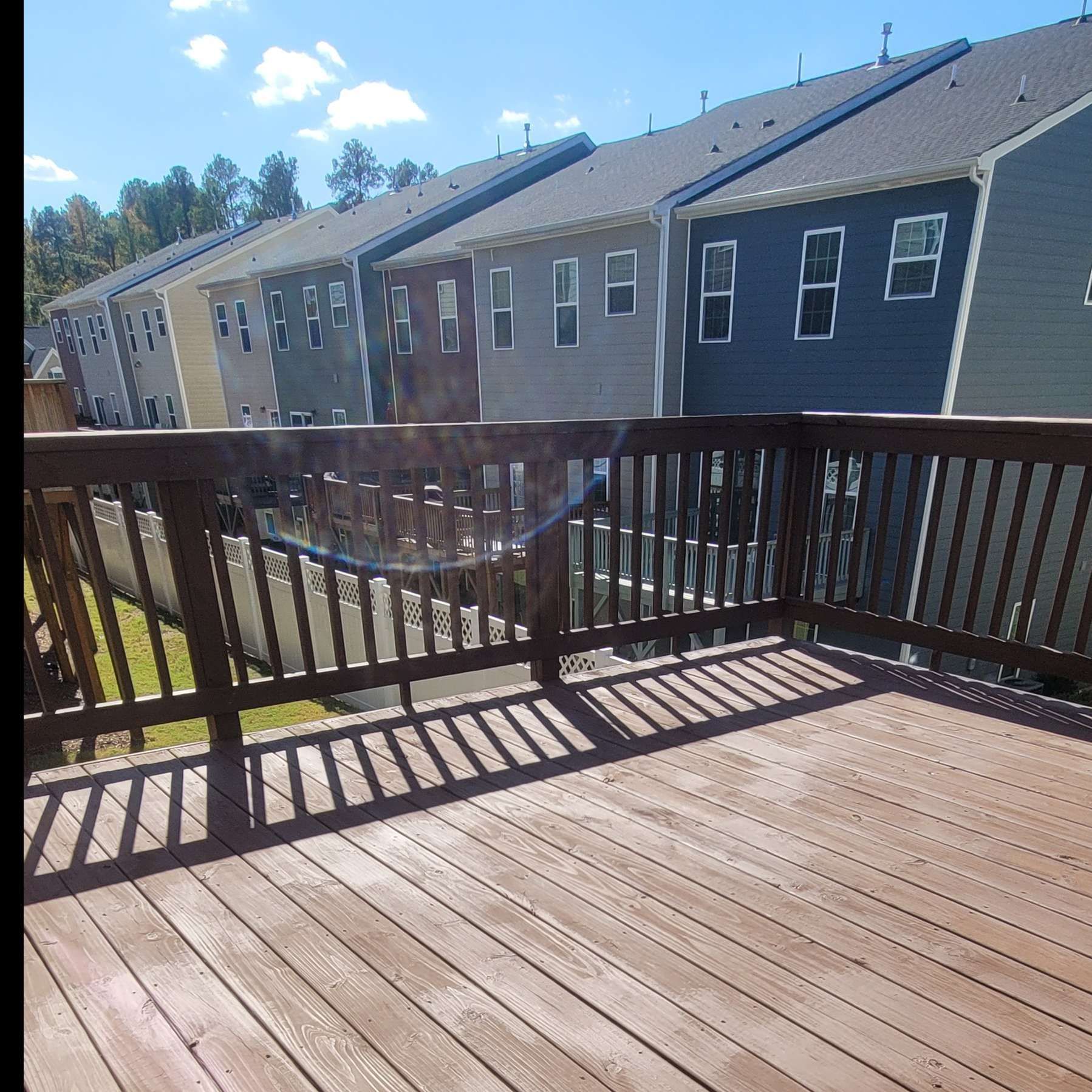 Wooden deck with railing, overlooking row of townhouses with various colored siding, under a blue sky.