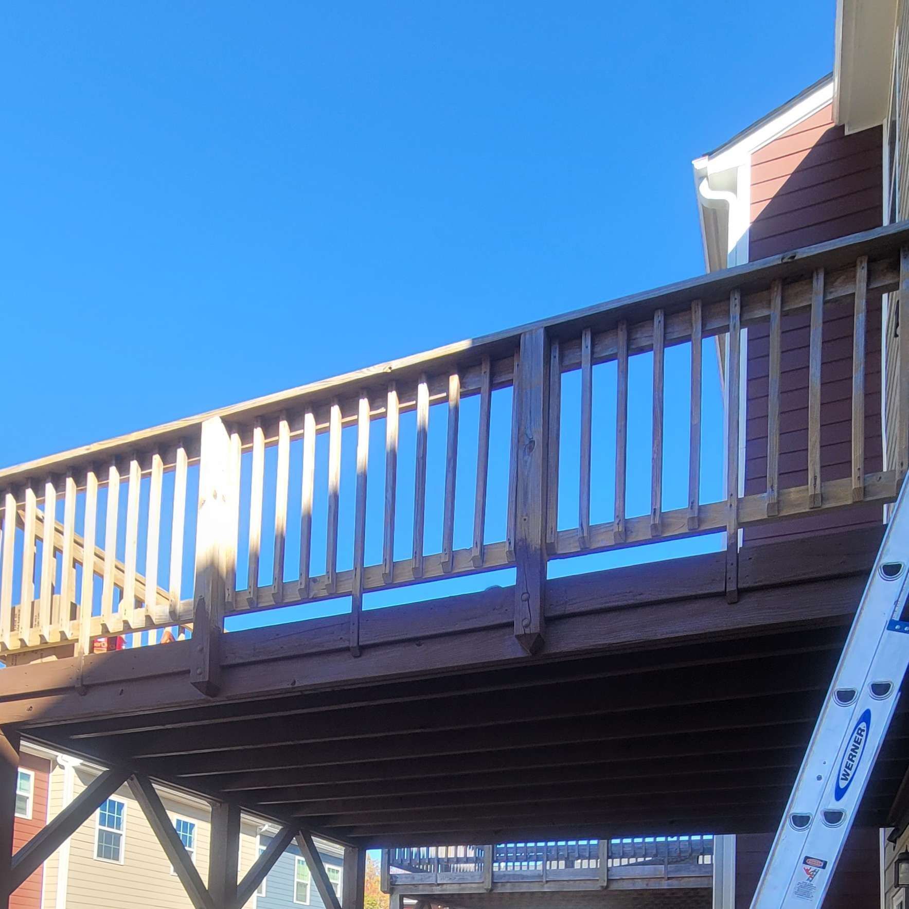 Wooden deck with railing attached to a building under a bright blue sky.