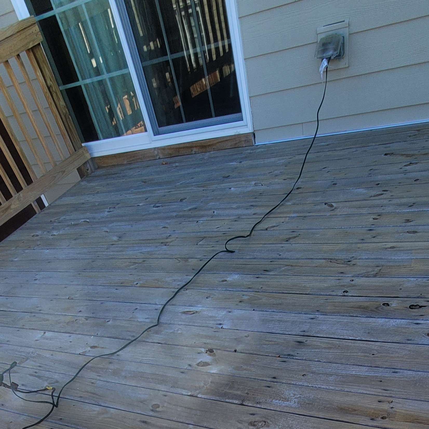 Wooden deck with a sliding door and an electrical cord running across it.