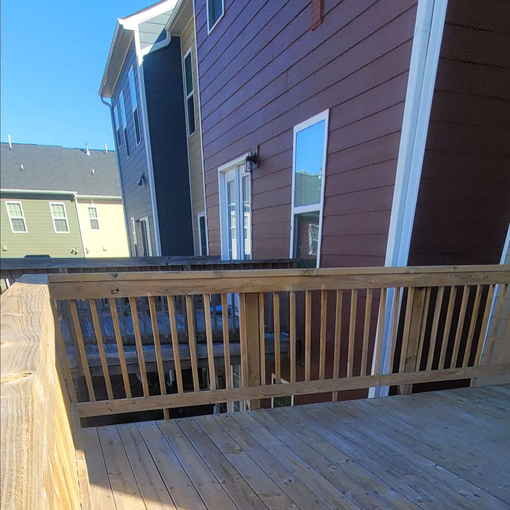 Wooden deck with a railing in front of a two-story building with a red and blue exterior under a blue sky.