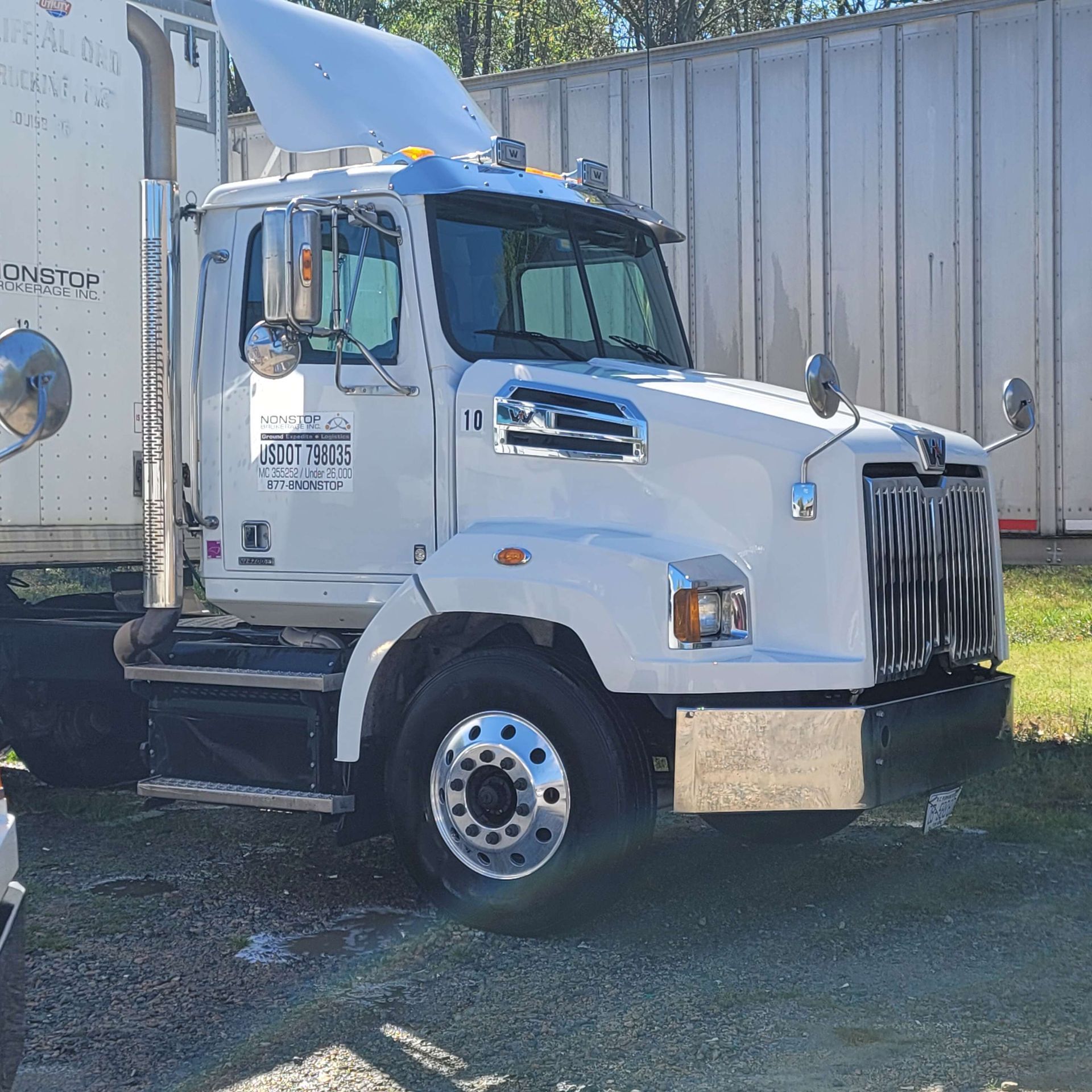 White semi-truck parked outdoors with a trailer attached, in front of a warehouse-like structure