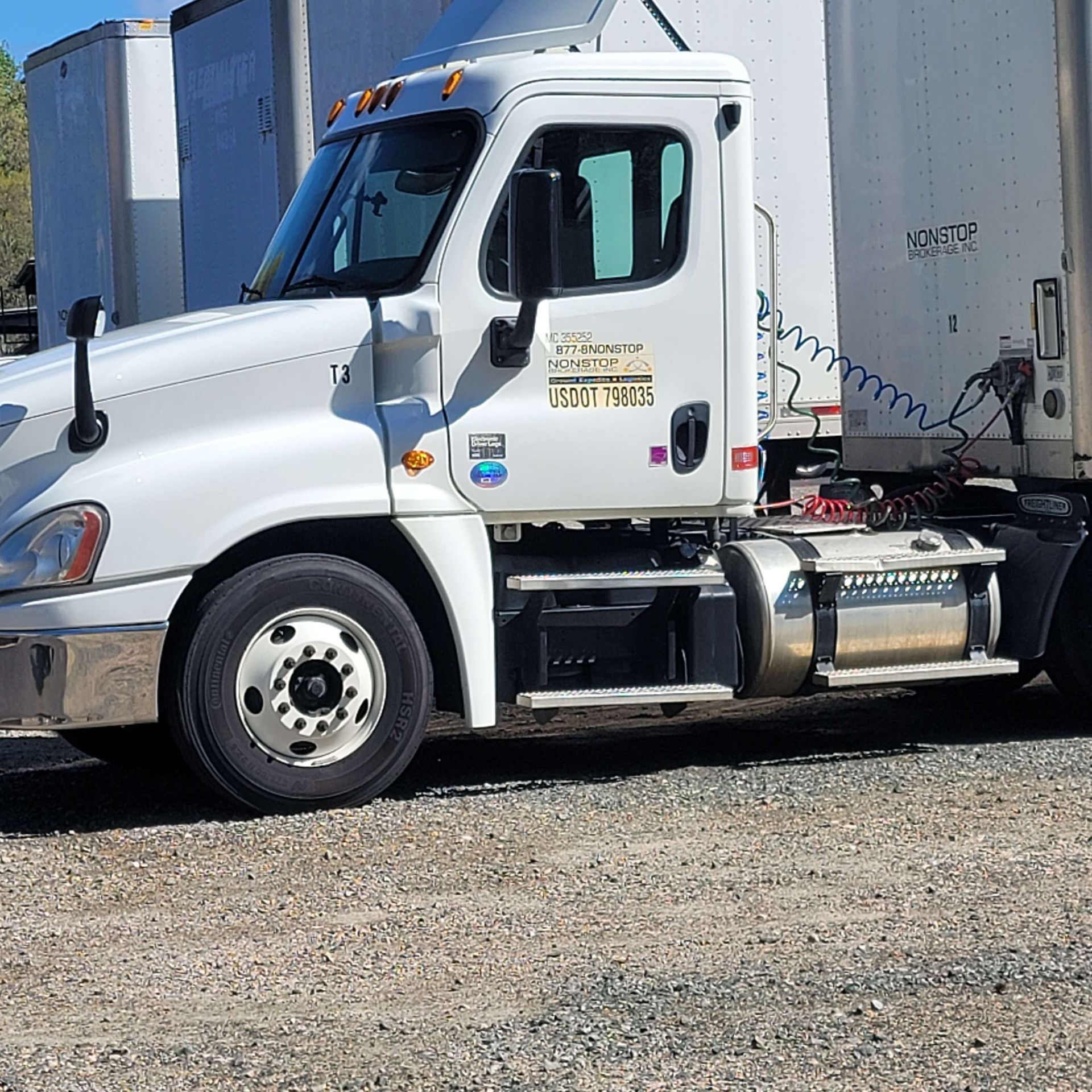 White semi-truck parked on gravel, driver's side view