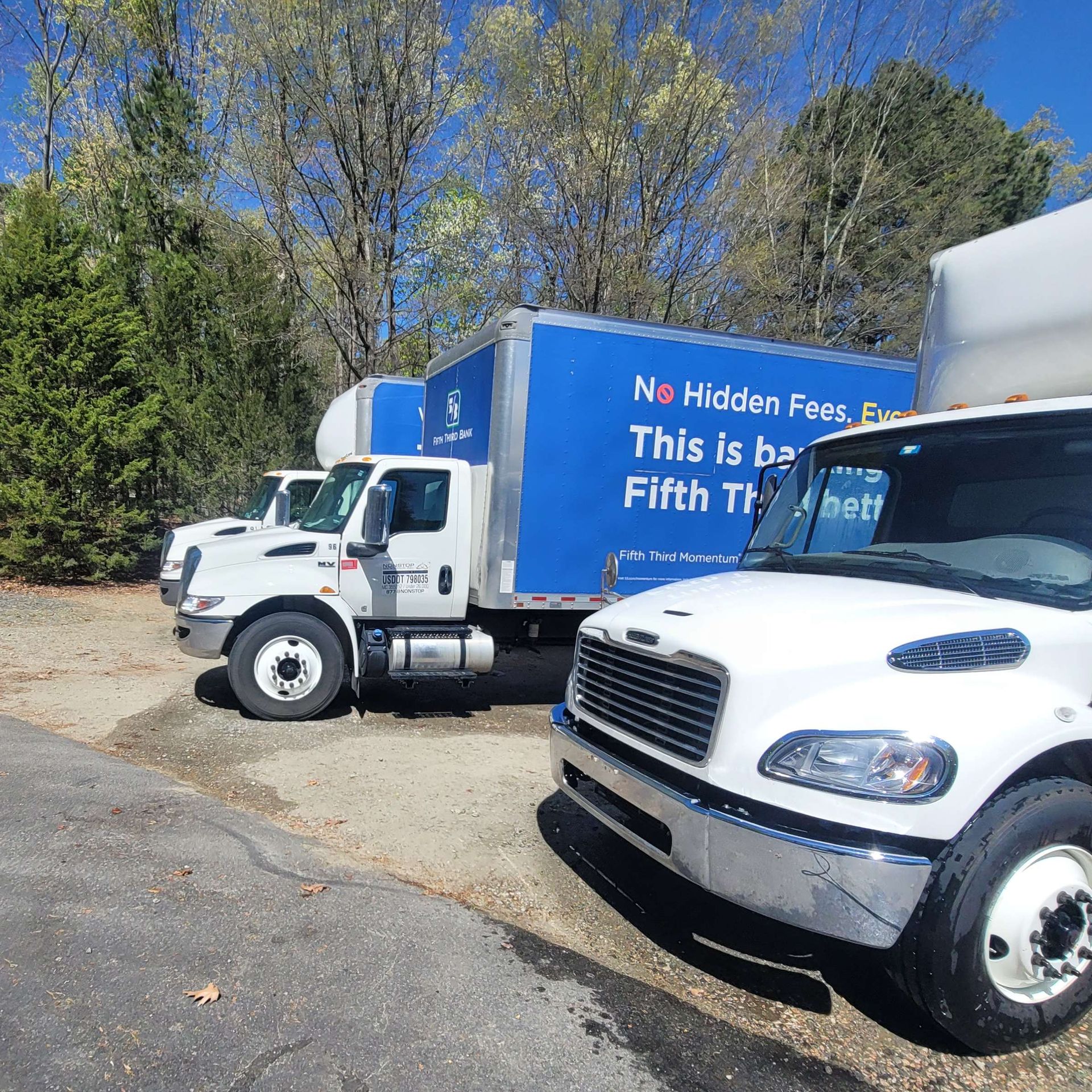Three white moving trucks parked outdoors with trees in the background.