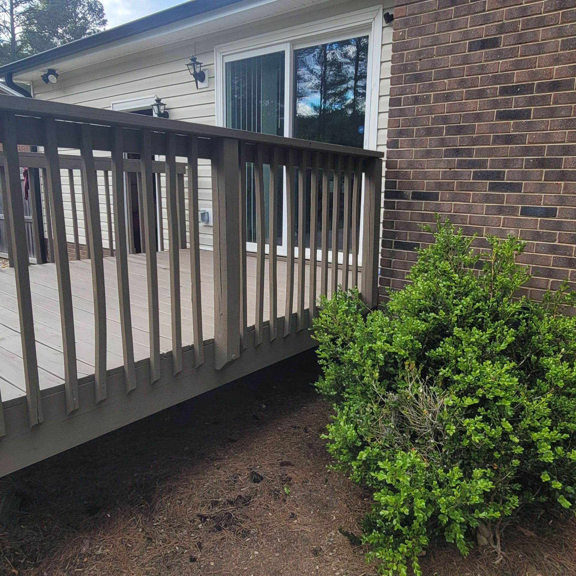 Wooden deck with railing next to a brick house