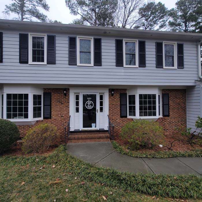 Two-story townhouse with gray siding, brick front, black shutters, and a white front door.