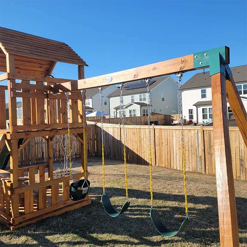 Wooden swing set in a backyard with two swings, a blue sky, and a wooden fence.